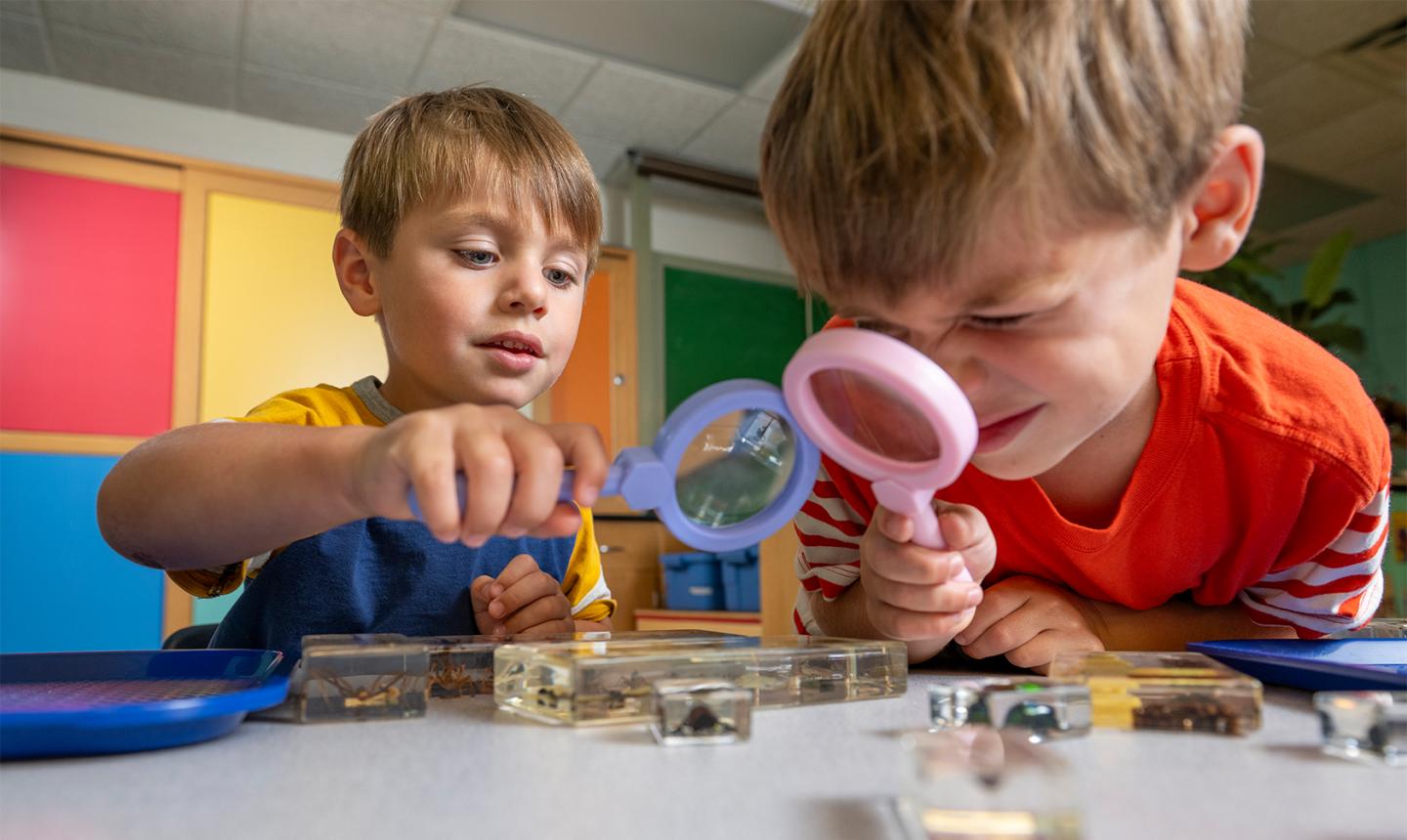 Two kids looking through magnifying glasses at a table of objects